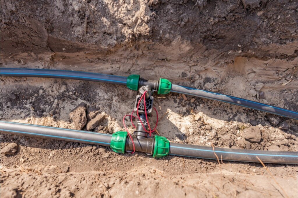 Magnetventil mit Steuerkabel zwischen zwei Bewässerungsleitungen in einem offenen Graben